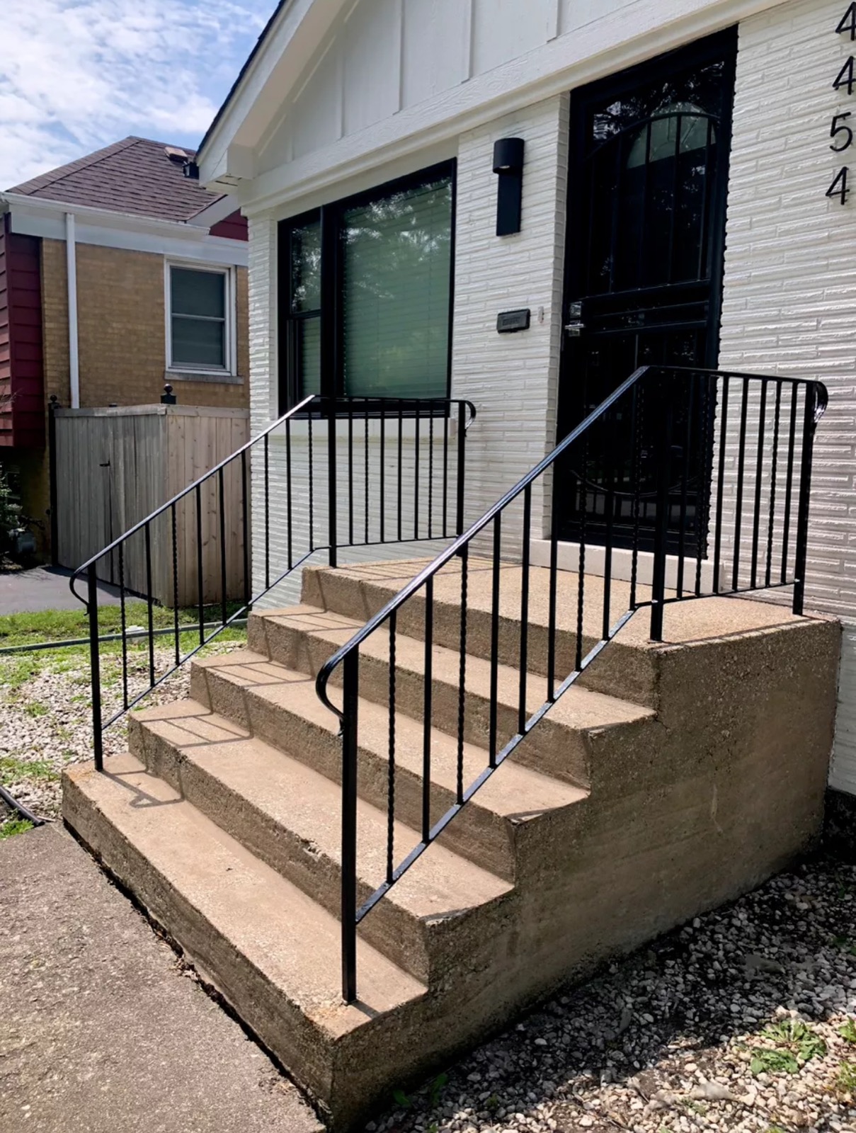 Black steel front entry railings installed on wide concrete residential steps.