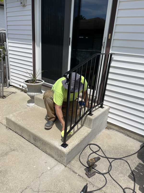 Custom porch handrail installed on front concrete steps with black steel finish.
