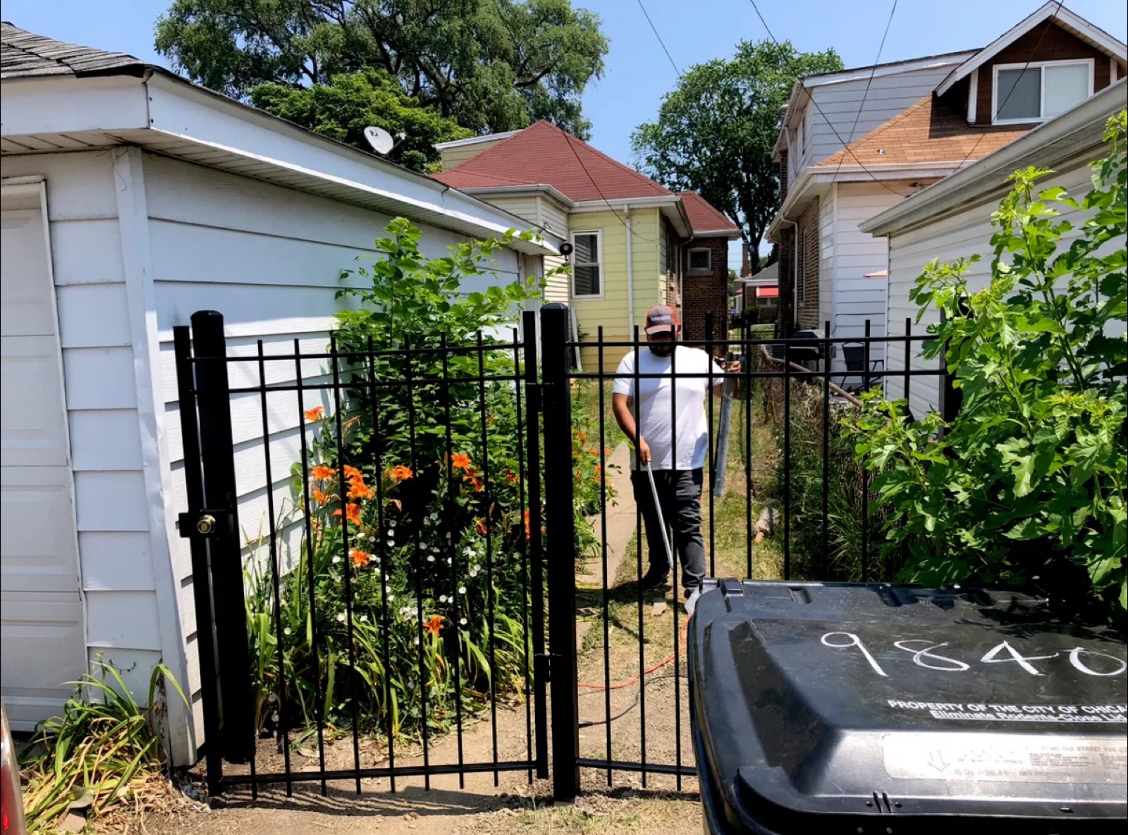 Custom black steel side-yard gate installed between a garage and residential walkway.