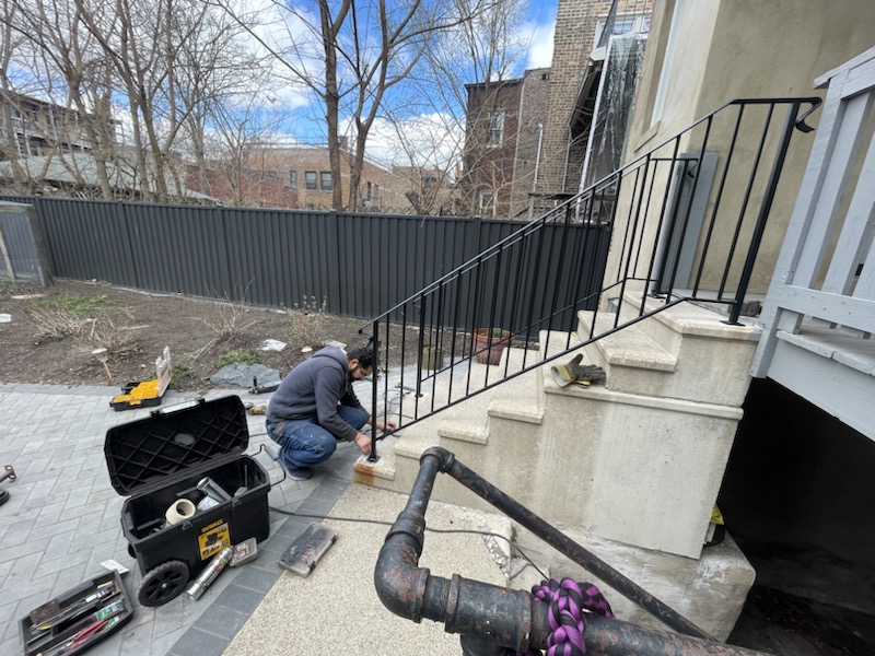 Exterior stair railing installation on concrete steps for a residential property.